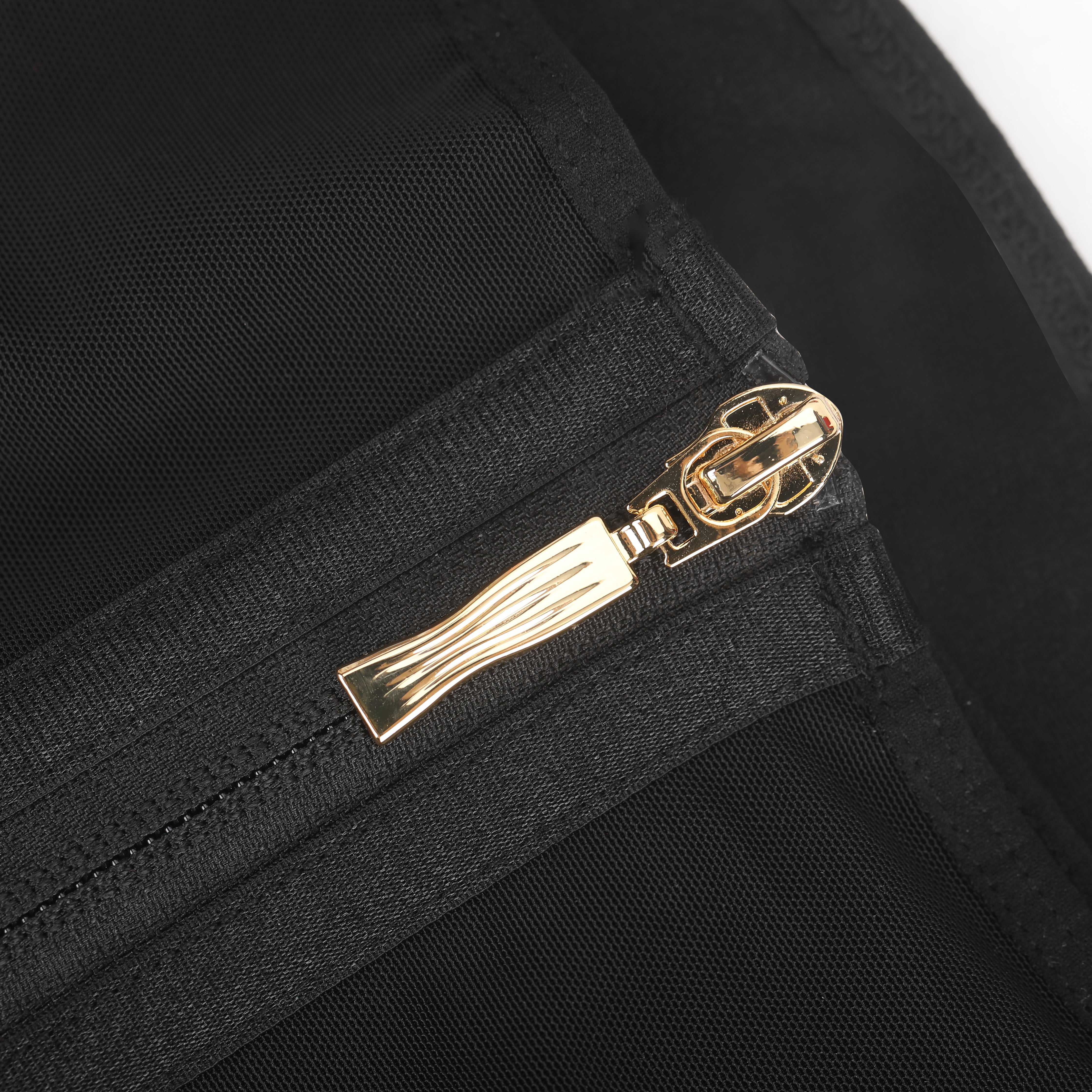 Close-up of a gold zipper pull on black fabric